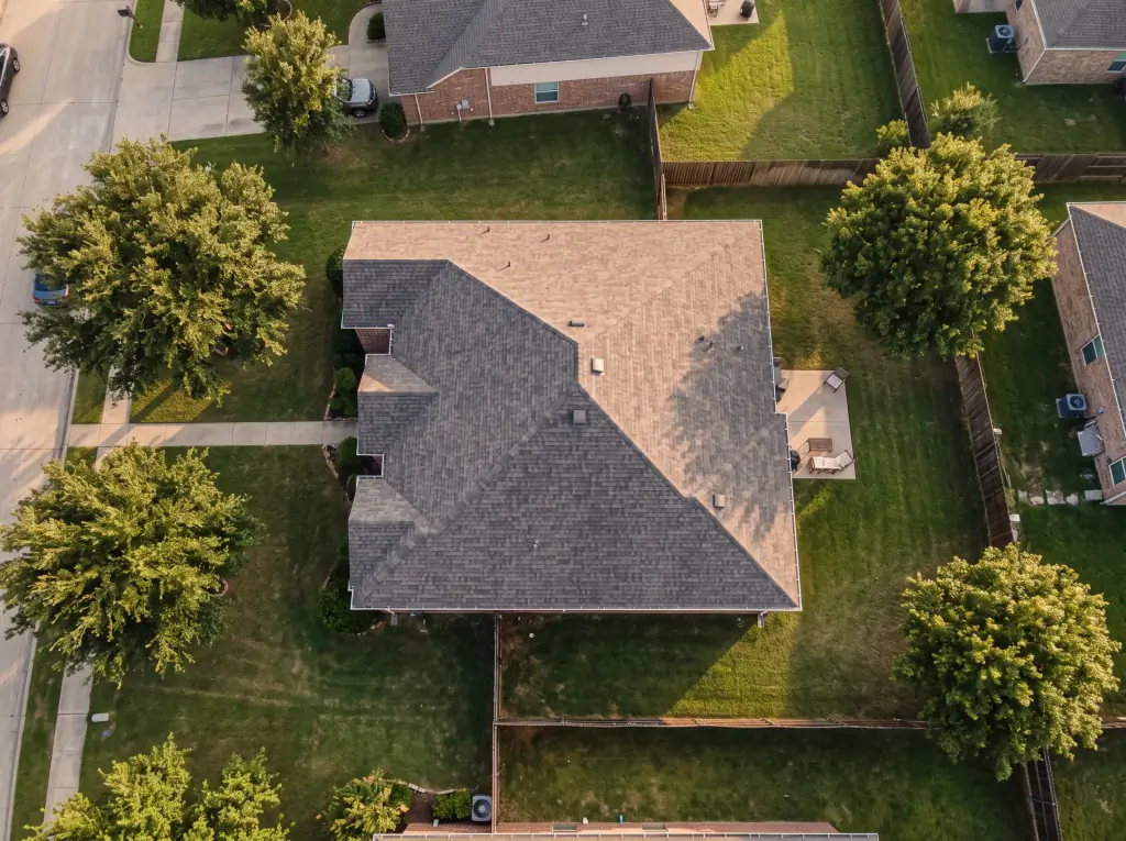 Aerial drone view of a hip roof being inspected in a residential neighborhood
