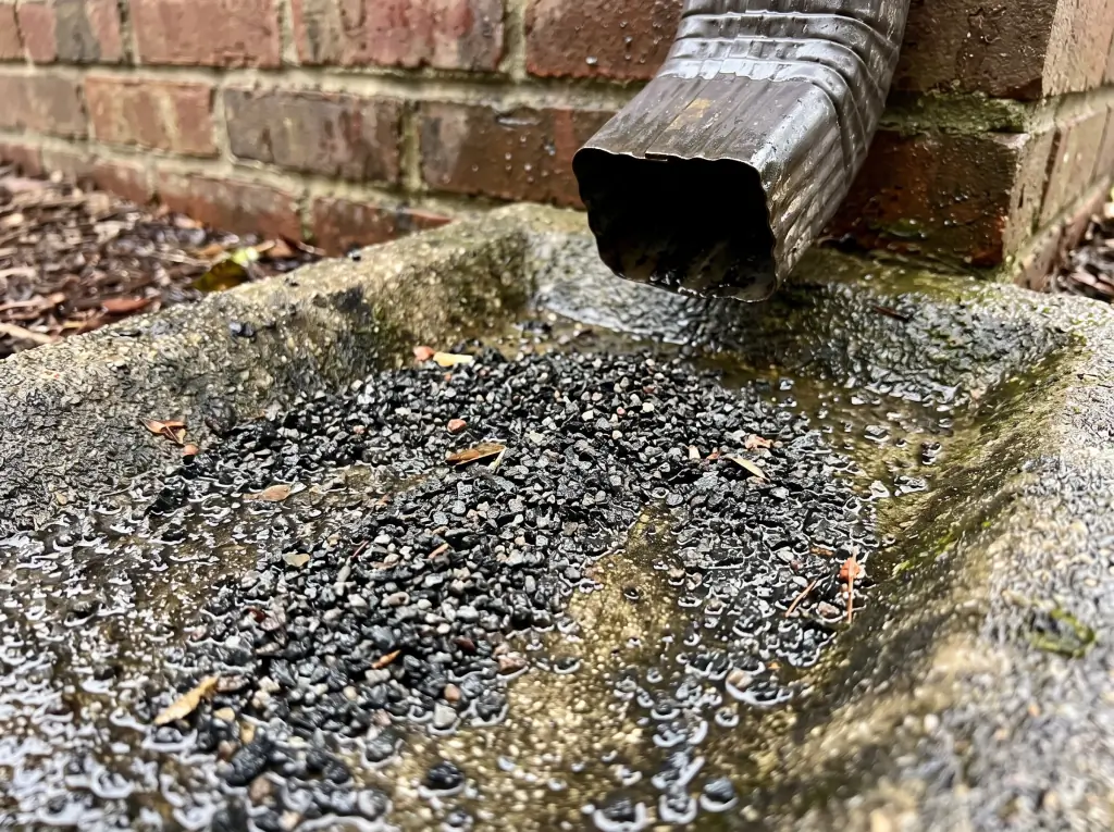 Shingle granules washed out of a downspout onto a splash block